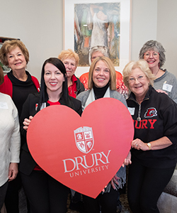 Drury alumni standing with a ϲʿ heart.